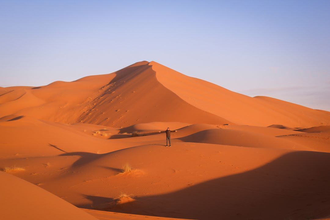 dunas desierto y chica de lejos con brazos abiertos mirando a la cámara en marruecos